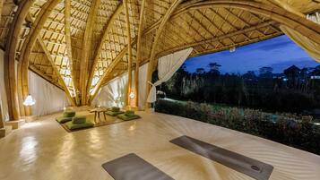 Amplia habitación con techo de bambú, cojines verdes y esterillas de yoga.