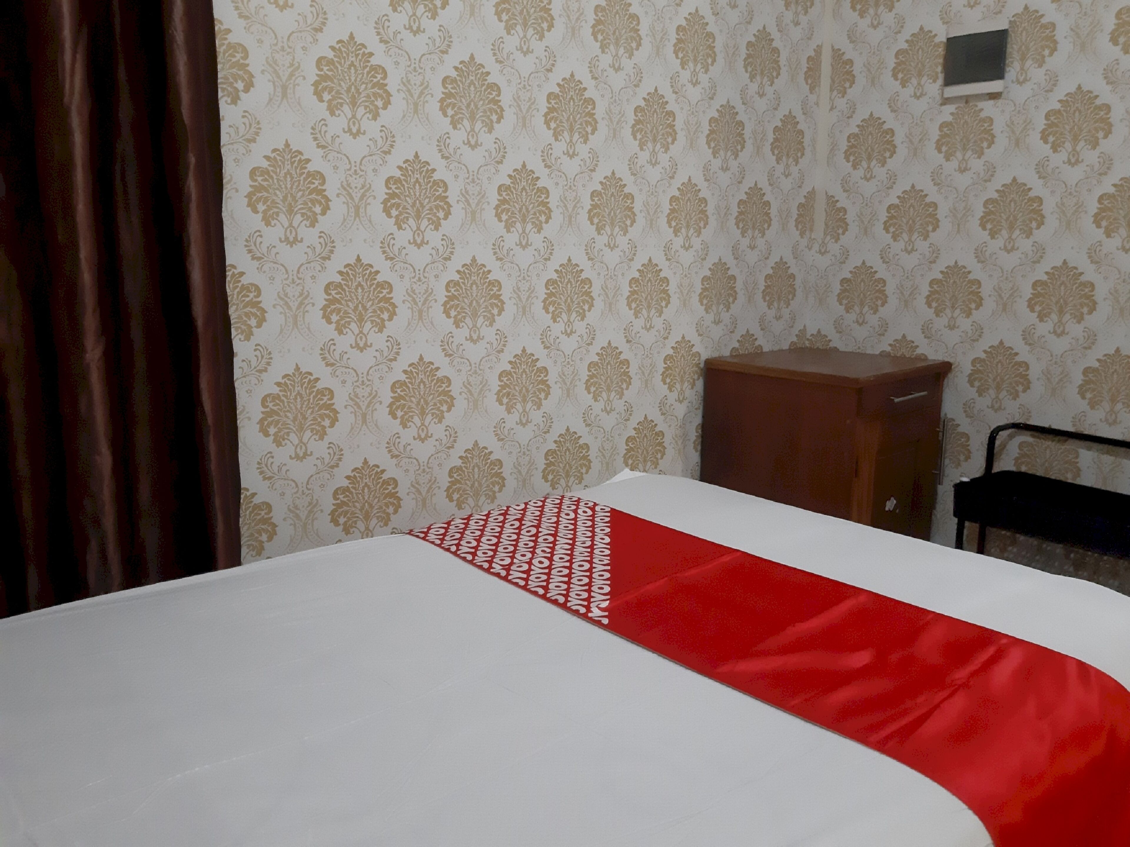 A room with a bed, a wooden cabinet, and a patterned wallpaper.
