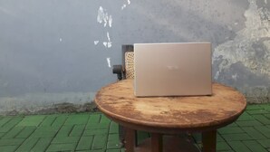 Een laptop op een ronde houten tafel tegen een verweerde muur.