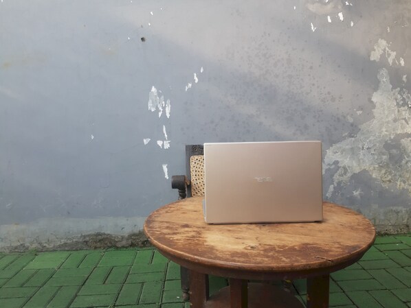 A laptop on a round wooden table against a weathered wall.