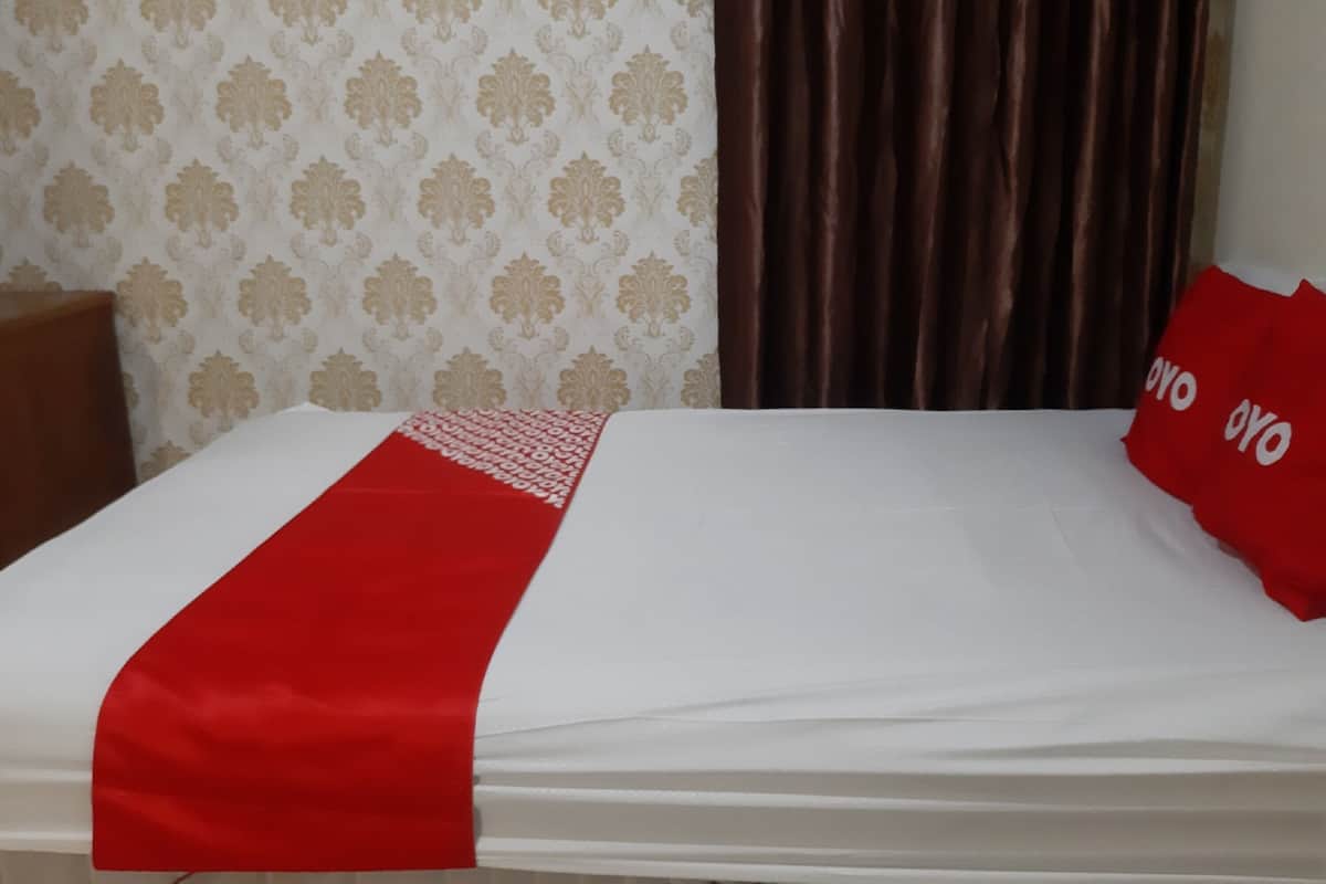 Een hotelkamer met een bed, een rood-wit beddeken, behang met een patroon en een bruin gordijn.
