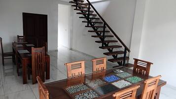 A dining area with a glass-top table, wooden chairs, and a staircase with wooden steps.