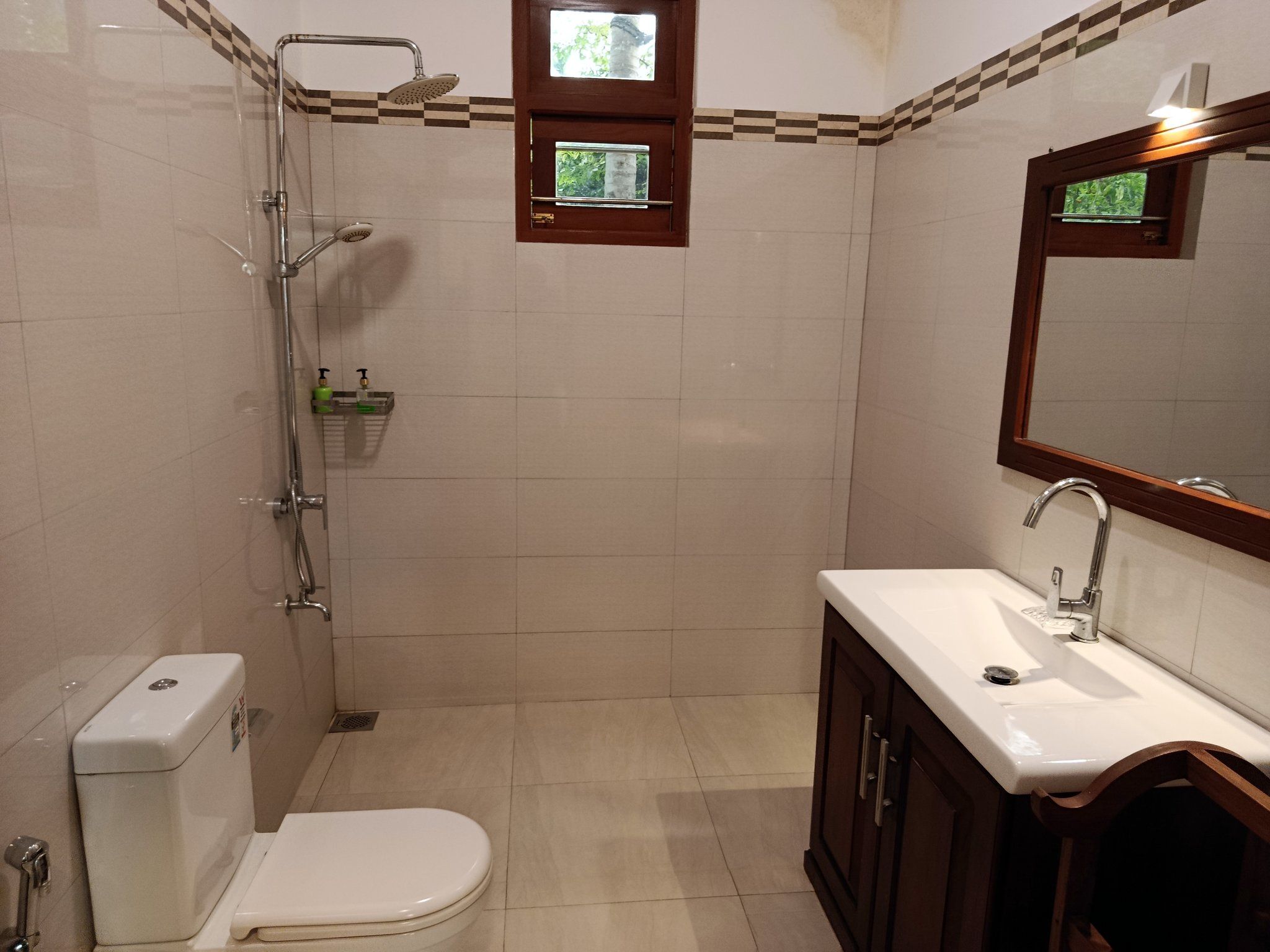 Un baño con inodoro, lavamanos, espejo, ducha y una pequeña ventana.