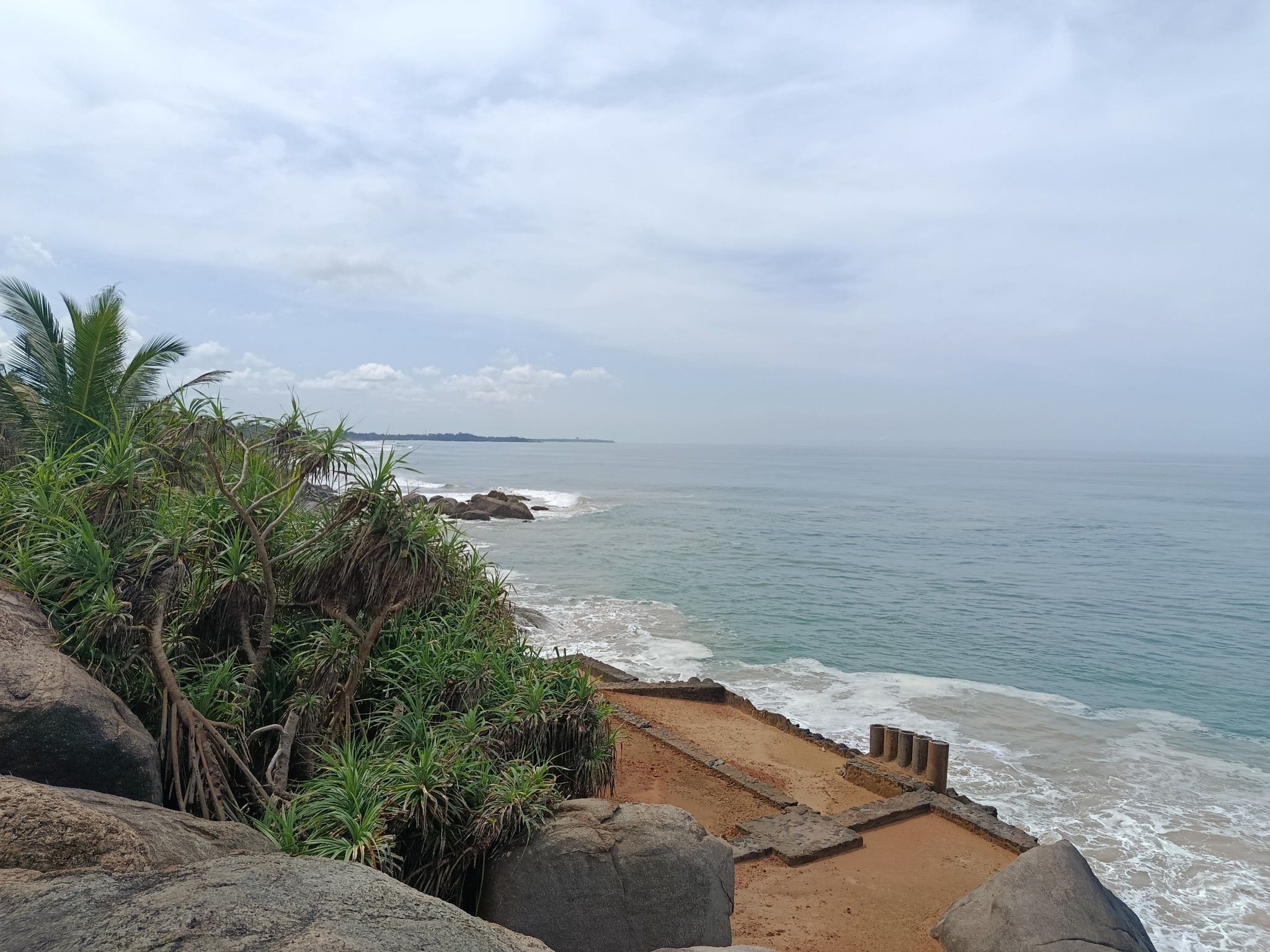 A coastal landscape with a sandy beach, rocky outcrops, and dense vegetation.