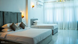 A modern hotel room with two beds, a large window with white curtains, a wall-mounted air conditioner, and a ceiling light fixture. - Piyum Villa Kosgoda (Kosgoda)