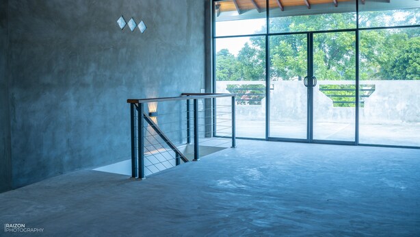 A spacious interior with a concrete floor, a staircase with metal railings, and large glass doors leading to an outdoor area with greenery. - Piyum Villa Kosgoda (Kosgoda)