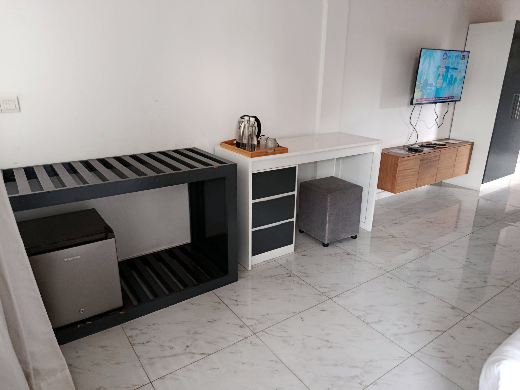 A modern, minimalist room with a bed, a desk, a small fridge, a TV, and a wooden cabinet.