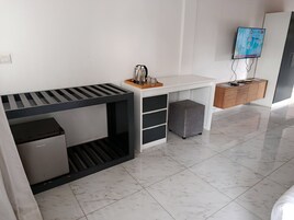 Una habitación moderna y minimalista con cama, escritorio, un refrigerador pequeño, televisor y un armario de madera.
