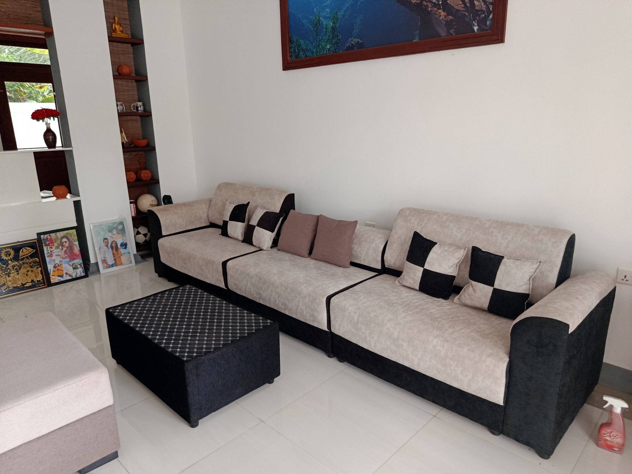 A modern living room with a sofa, a black ottoman, and a shelf with decorative items.