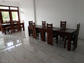 Un comedor con una gran mesa de madera y sillas, suelo de baldosas y ventana con vista a la vegetación.