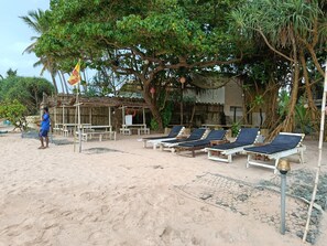 Un espace aménagé au bord de la plage, avec des chaises longues, un drapeau et une structure en bambou.