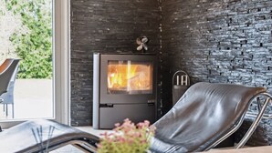A modern living room with a stone wall, a fireplace, a leather chair, and a dining table with flowers. - "Fidelia" - 400m from the sea by Interhome (Storvorde)