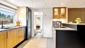 A modern kitchen with wooden cabinets, a black refrigerator, and a large island with a sink. - "Fidelia" - 400m from the sea by Interhome (Storvorde)