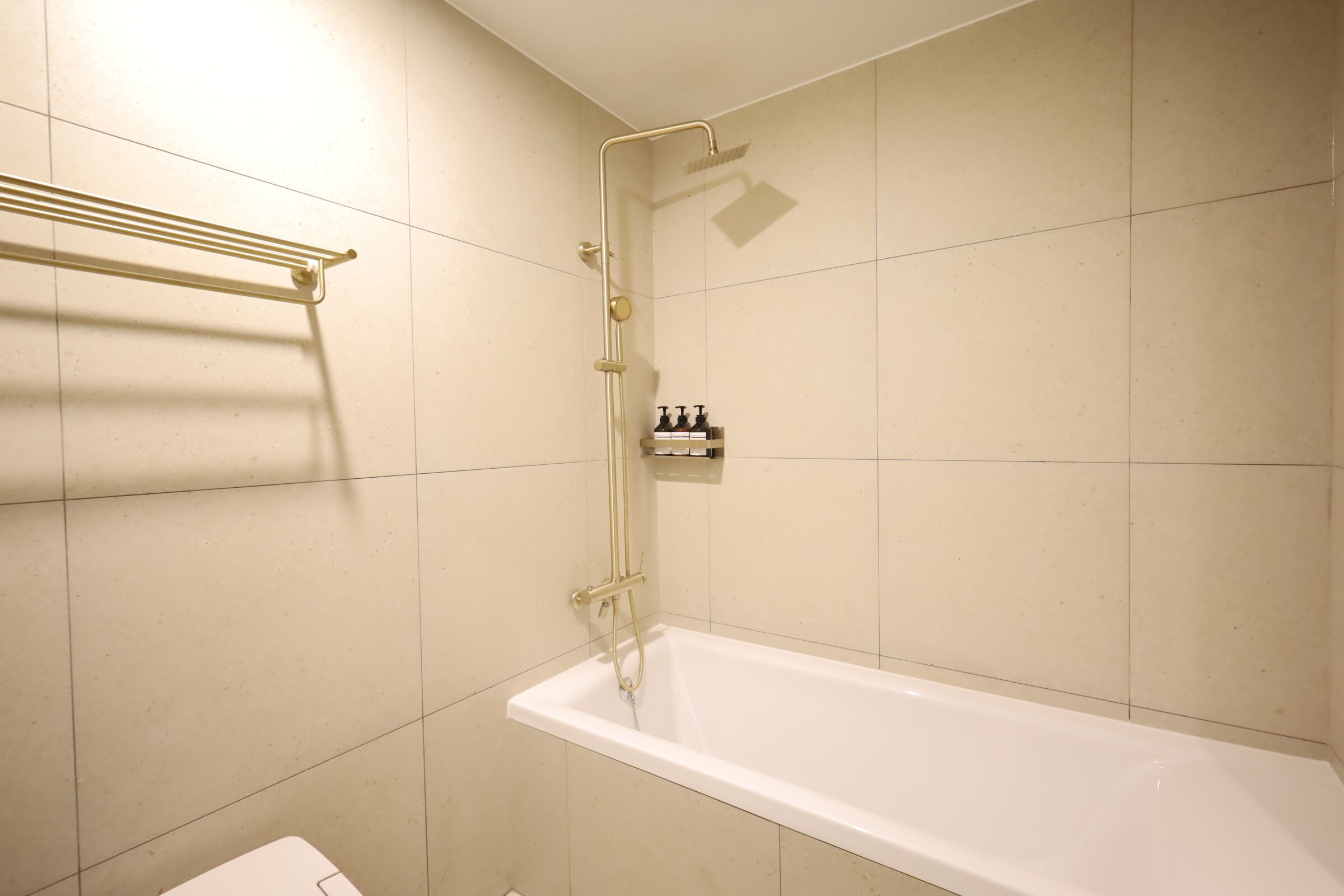 A bathroom with a white bathtub, a showerhead, and a towel rack.