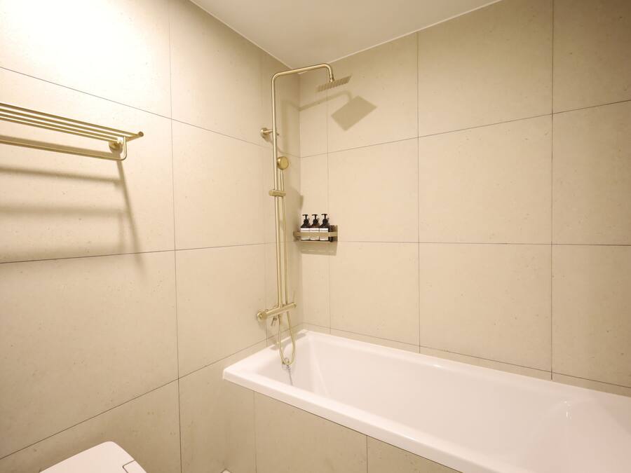 A bathroom with a white bathtub, a showerhead, and a towel rack.