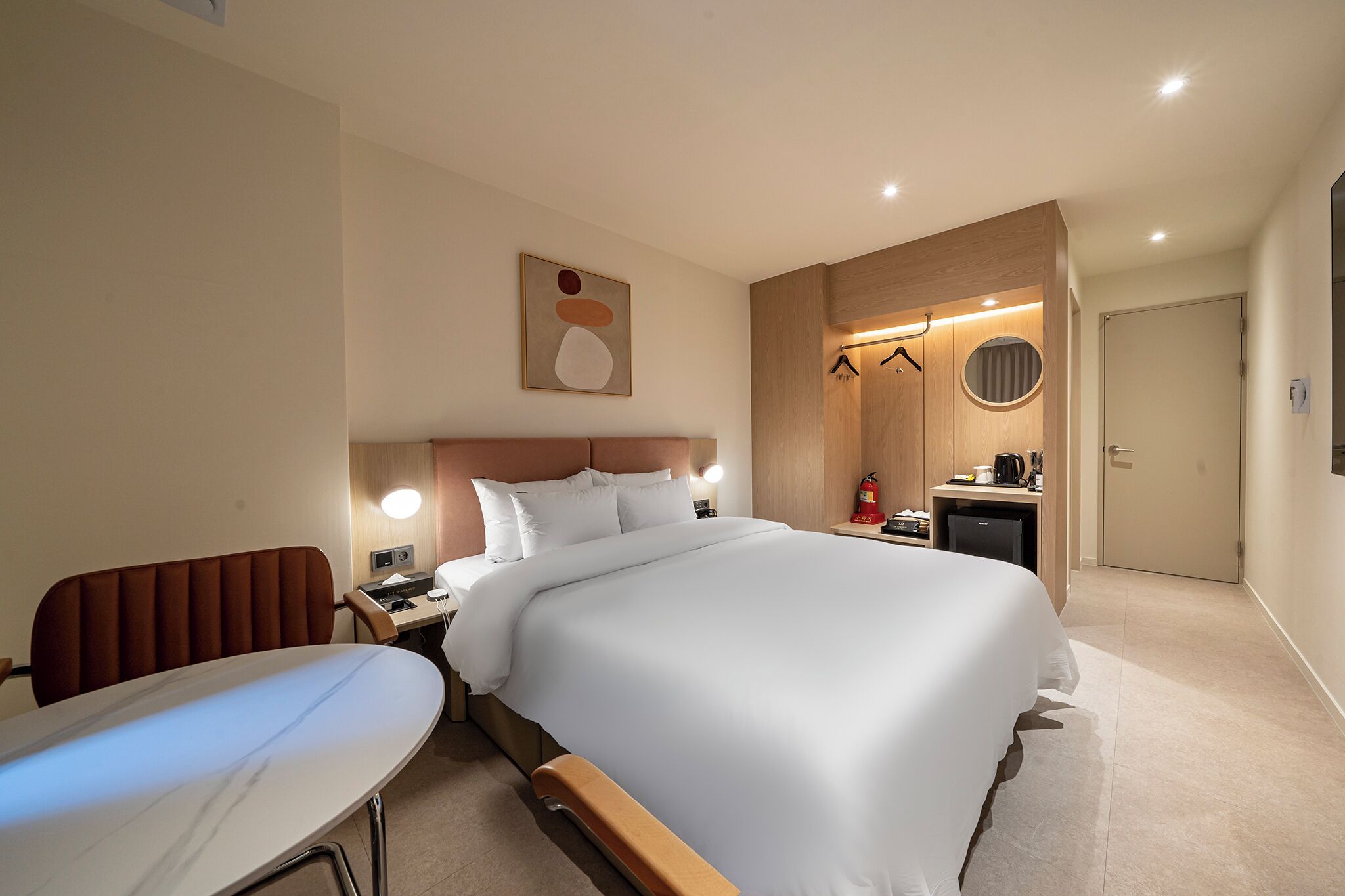 Habitación de hotel con una cama grande, un escritorio con una silla, una mesita, un armario y un espejo.