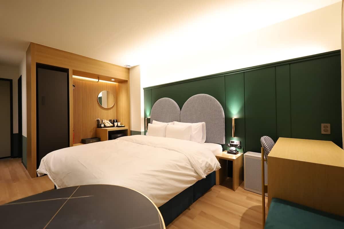 A modern hotel room with a large bed, bedside tables, a desk, and a chair.