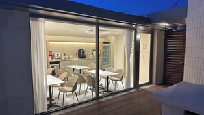 A modern dining area with glass walls, a kitchen visible in the background, and a wooden deck outside. - H AVENUE  Jecheon Station (Jecheon)