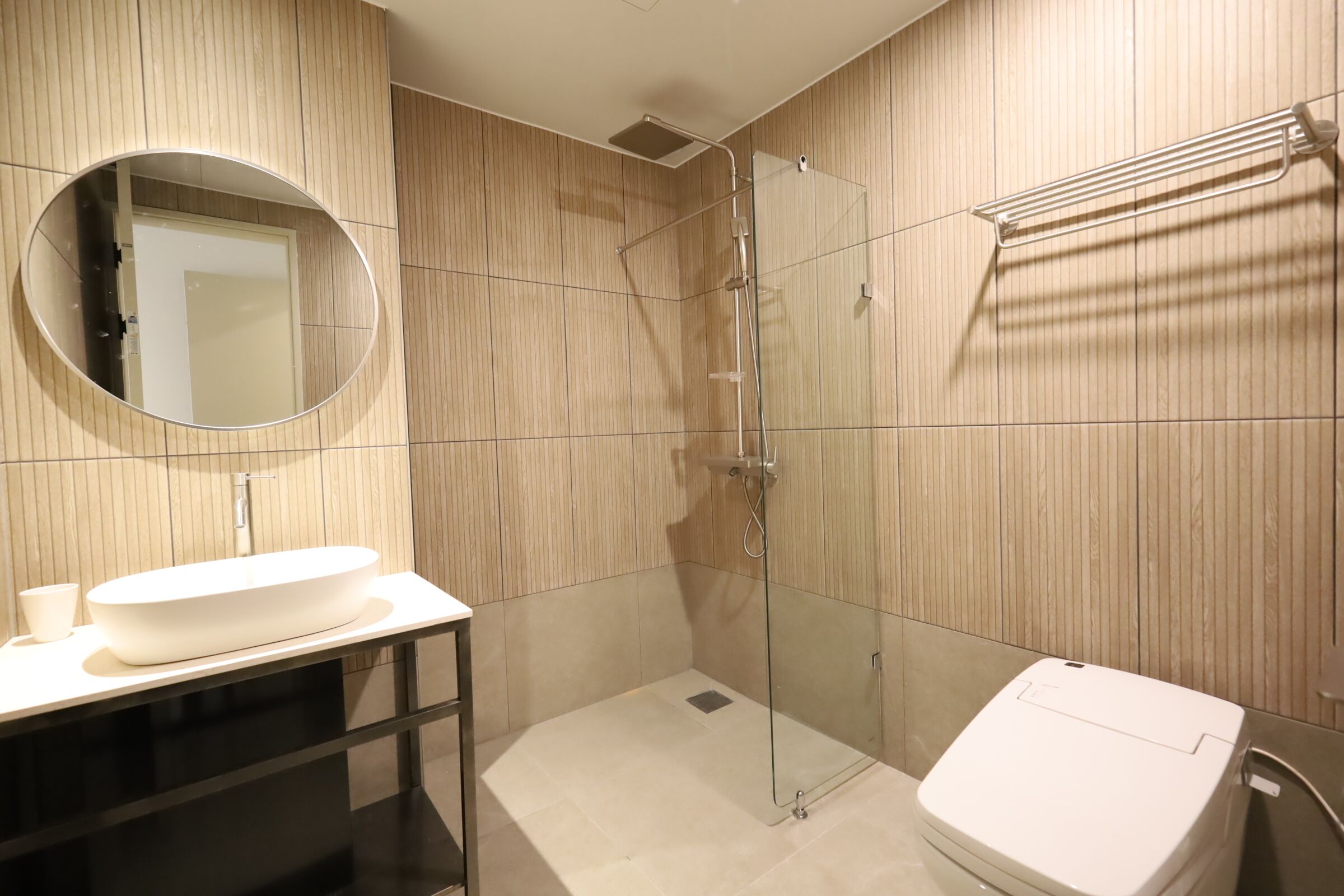 Une salle de bain moderne avec un grand lavabo ovale, un miroir rond, une douche à parois de verre et des toilettes blanches.