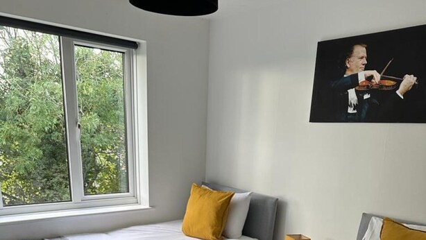 A hotel room with two beds, a window with a view of trees, a painting on the wall, and a bedside table with a lamp. - Black Door Malt - Huku Kwetu (Dunstable)