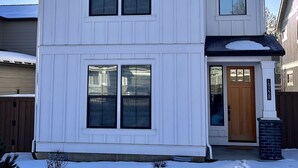 Une maison blanche à deux étages, avec une porte d’entrée, deux fenêtres au rez-de-chaussée et une porte de garage.