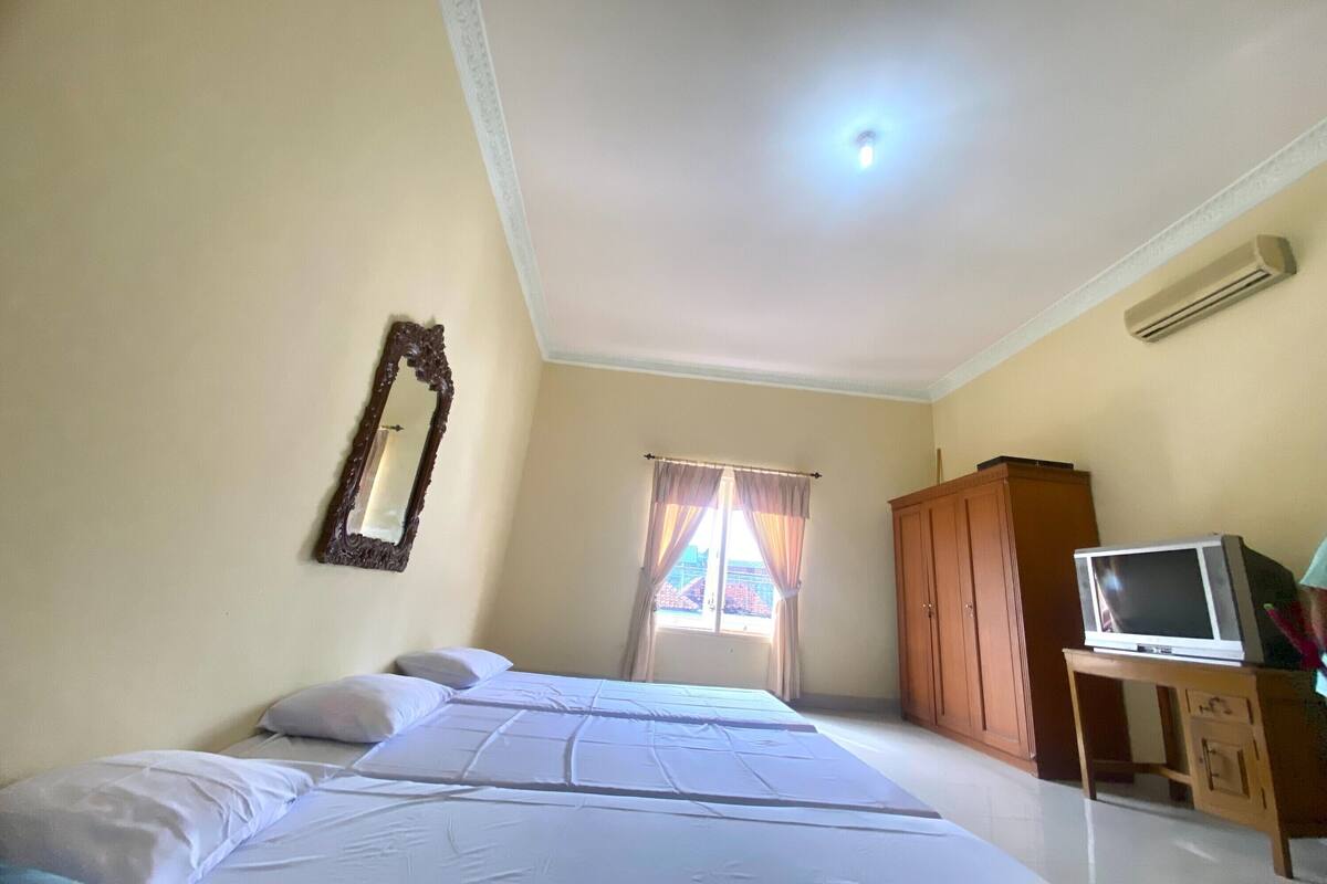 A bedroom with a bed, a mirror, a wardrobe, a television on a stand, and a window with curtains.