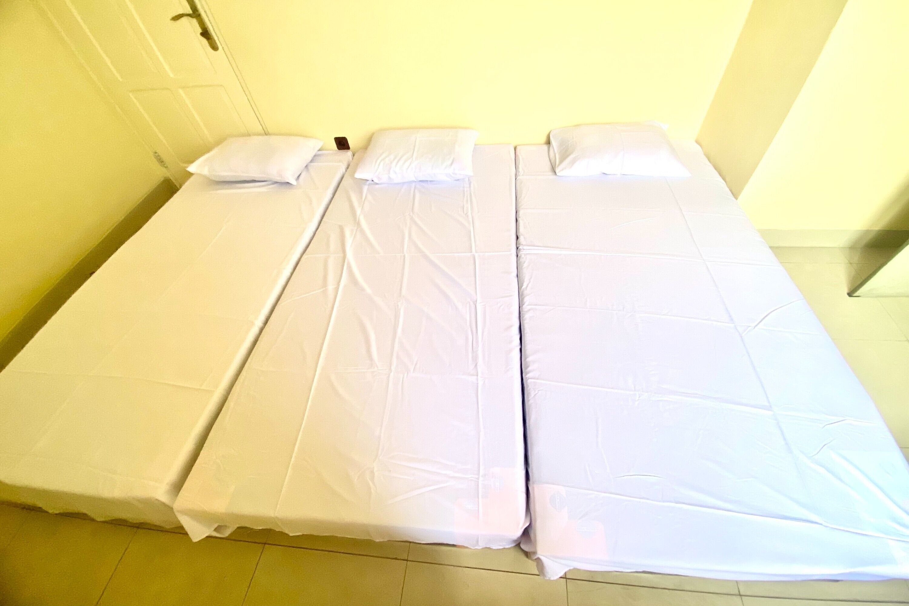 A single-bed room with a white bedspread, a door, and a light-colored floor.