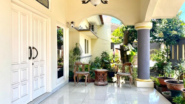 A covered outdoor area with a tiled floor, white doors, and a variety of potted plants. - Hotel O Kenzie Bunkbed Syariah (Klaten)