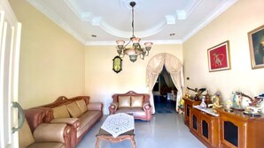 A spacious living room with a chandelier, a sofa, a coffee table, and a cabinet with decorative items. - Hotel O Kenzie Bunkbed Syariah (Klaten)