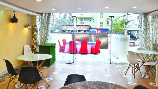 A room with a glass table and chairs, a green trash bin, and a view of a street with a shop. - Magadh Palace  (Danapur)