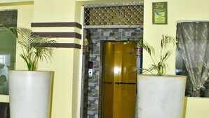 A reception area with a yellow wall, a reception desk, a large potted plant, a red mat, and an elevator. - Magadh Palace  (Danapur)