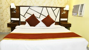 A neatly made bed with a wooden headboard, two nightstands with lamps, and a wall-mounted air conditioning unit. - Magadh Palace  (Danapur)