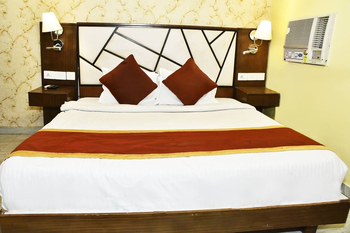 A neatly made bed with a wooden headboard, two nightstands with lamps, and a wall-mounted air conditioning unit.