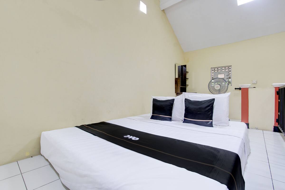 A neatly arranged bedroom with a bed, pillows, a bedside table, and a wall-mounted fan.