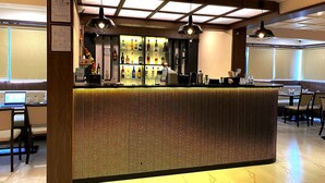 A bar area with a counter, bar stools, and a seating area with tables and chairs. - The Grand Sarovar Inn and Suites (Rajgurunagar)