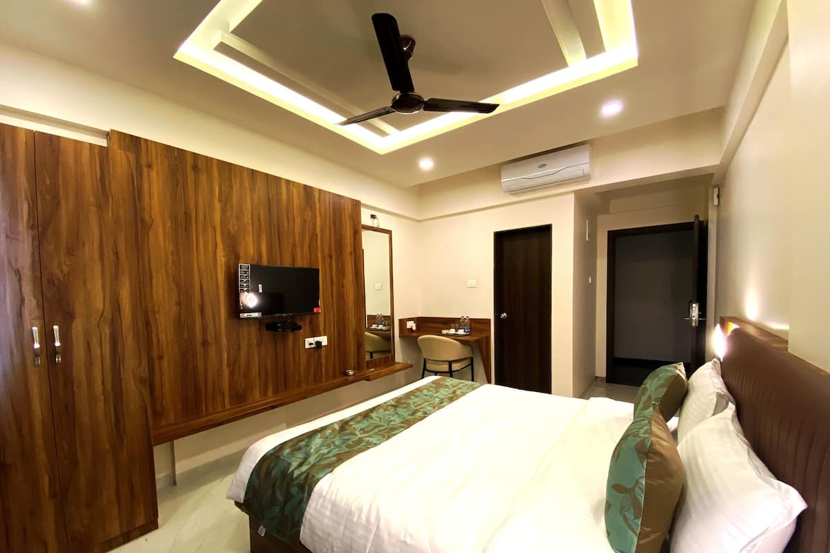 Une chambre d’hôtel moderne avec un grand lit, un téléviseur fixé au mur et un ventilateur de plafond.