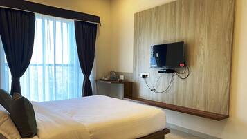 A hotel room with a large bed, a TV mounted on the wall, a small table with a water bottle, and a window with curtains.