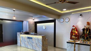 A reception area with a marble reception desk, a ceiling fan, and wall clocks indicating New Delhi and Tokyo. - The Grand Sarovar Inn and Suites (Rajgurunagar)