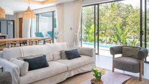 A modern living room with a sofa, armchair, and dining area. - Modern 3 Bedroom Villa - KBR16 (Koh Samui)