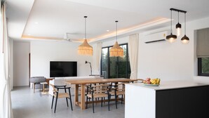 A modern kitchen with a central island, dining area, and a TV. - Modern 3 Bedroom Villa - KBR16 (Koh Samui)