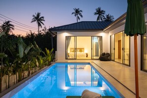 Een moderne villa met een zwembad, een slaapkamer met een groot bed en gordijnen, en uitzicht op palmbomen.