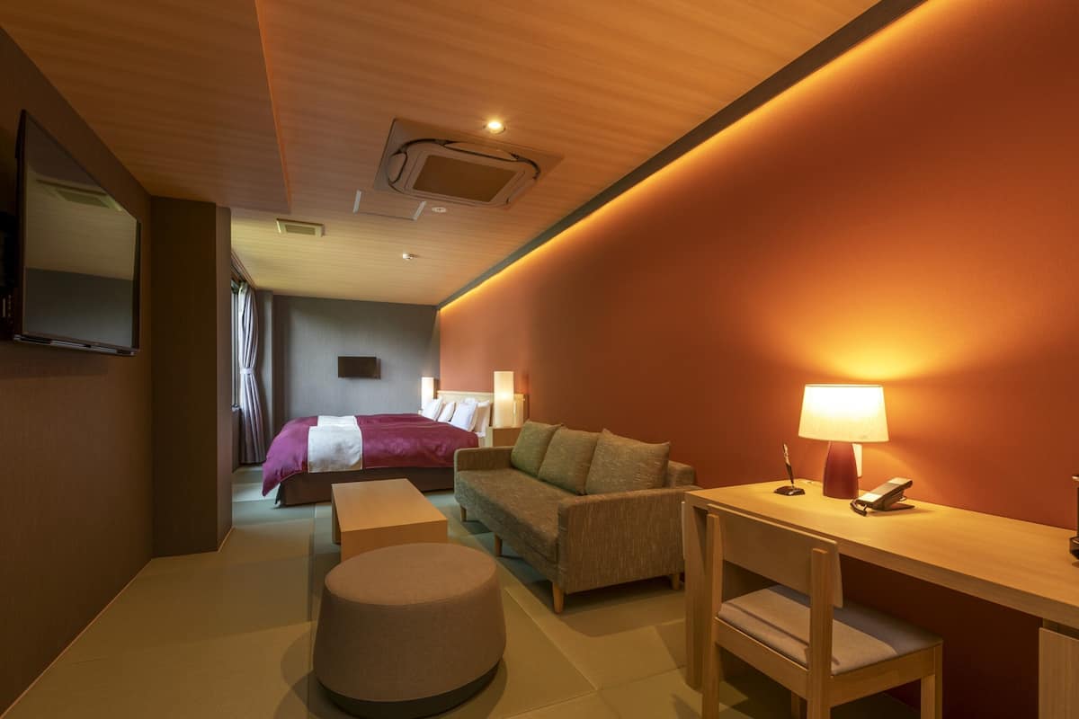Ein Hotelzimmer mit Bett, einer Couch, einem Schreibtisch mit Lampe und einem an der Wand befestigten Fernseher.