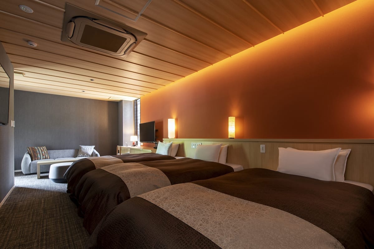 Ein Hotelzimmer mit zwei Betten, einem Schlafsofa, einem Fernseher und einem Schreibtisch mit Lampe.