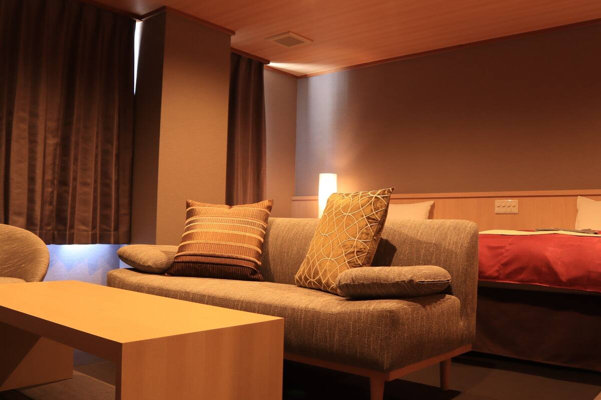 Ein modernes Hotelzimmer mit einer Couch, einem Holztisch und einem Bett mit roter Decke.