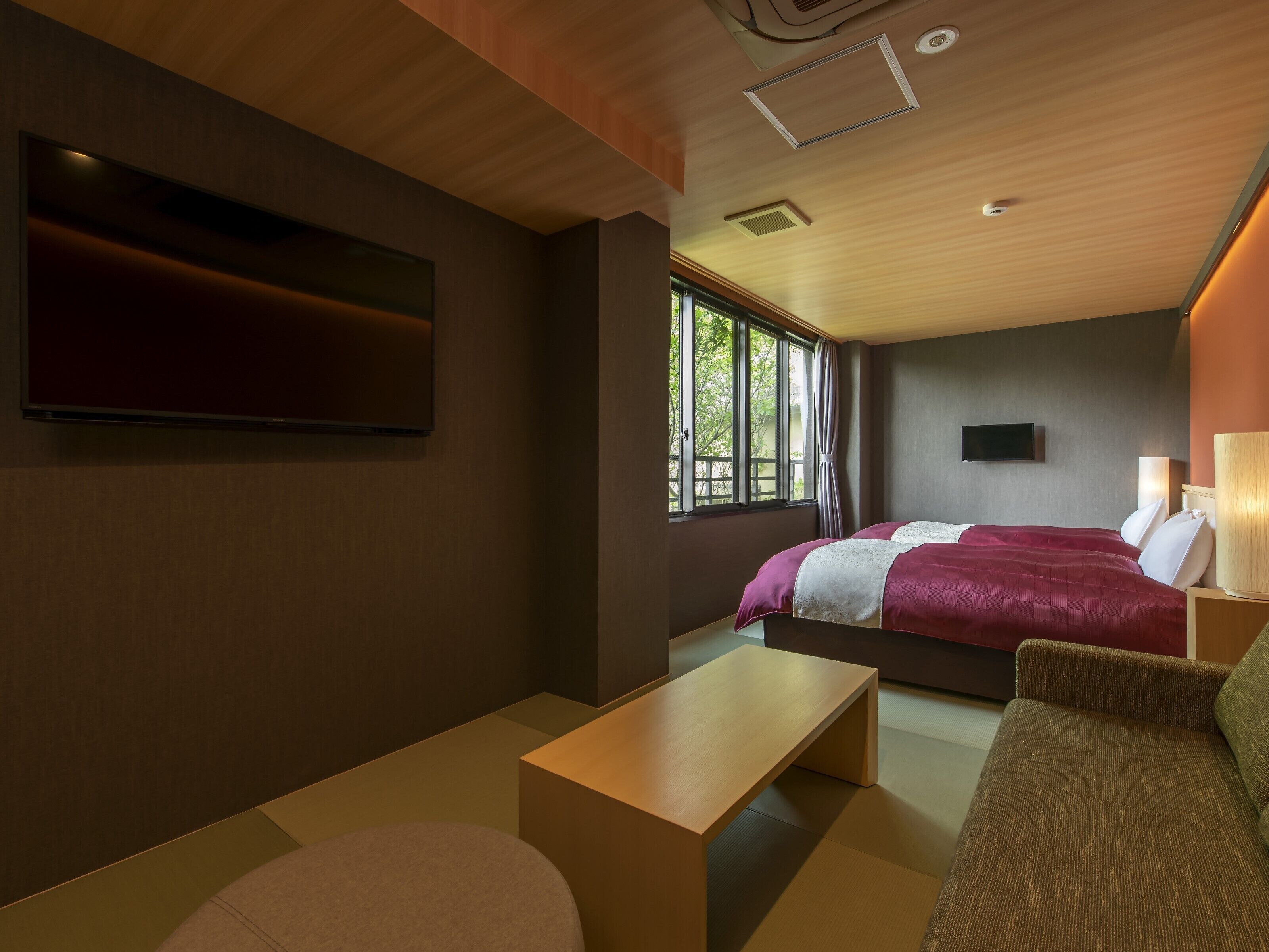 A modern hotel room with a bed, a TV, a desk, and a sofa.