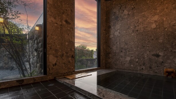 A spa room with a large window, a stone wall, and a black tiled floor. - Tamana Onsen Kura no Sato (Tamana)