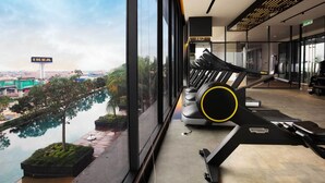 A gym with a treadmill and stationary bikes, overlooking a cityscape with an IKEA sign visible outside. - Continew by Plush (Kuala Lumpur)