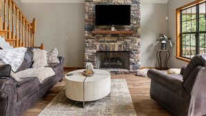 Una sala de estar con chimenea de piedra, un televisor de pantalla plana y dos sofás de cuero.