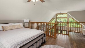 Un dormitorio con una cama grande, un ventilador de techo, una mesita de noche y vistas a un balcón con baranda de madera.