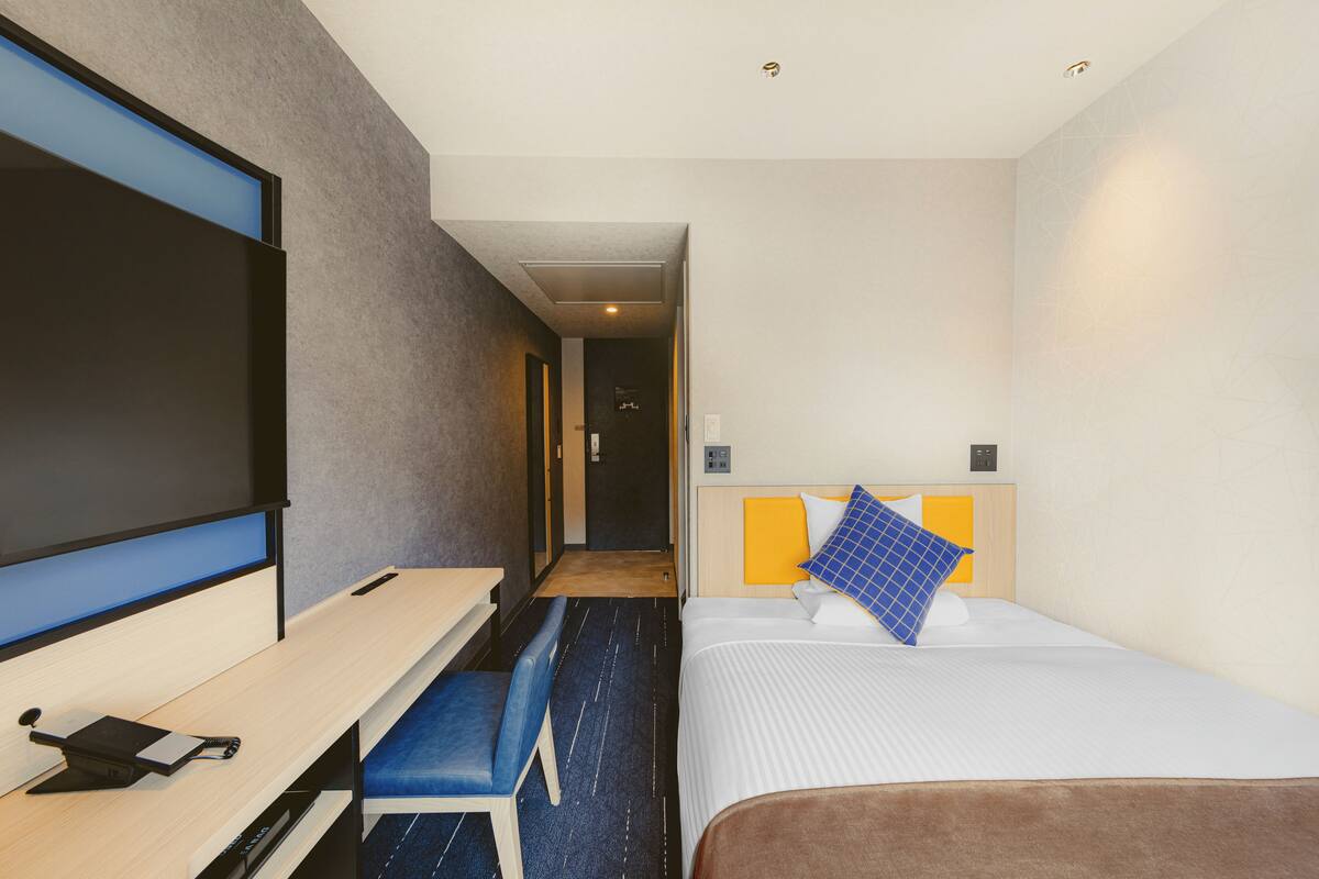 Ett hotellrum med en säng, ett skrivbord, en stol och en tv.